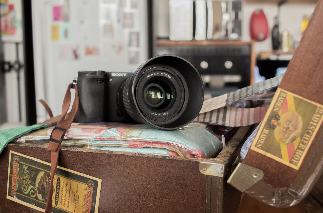 A modern camera with lens rests on a vintage suitcase in a cozy indoor setting.
