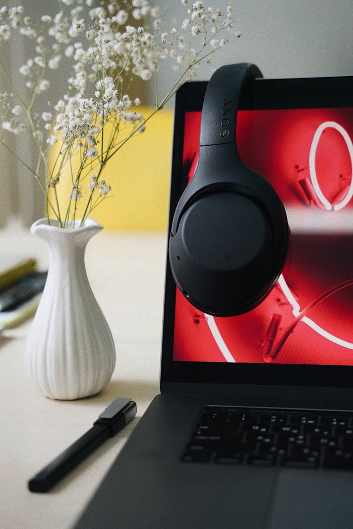 A sleek laptop with black headphones and a vase with flowers create a modern workspace setting.